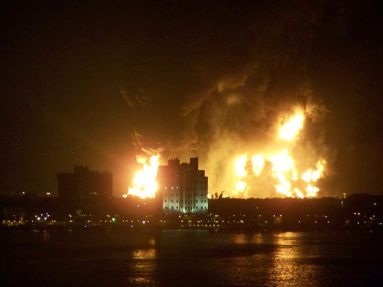 Night view of a refinery explosion with flames and smoke billowing from the facility, photographed from across a bay / Wikimedia Commons