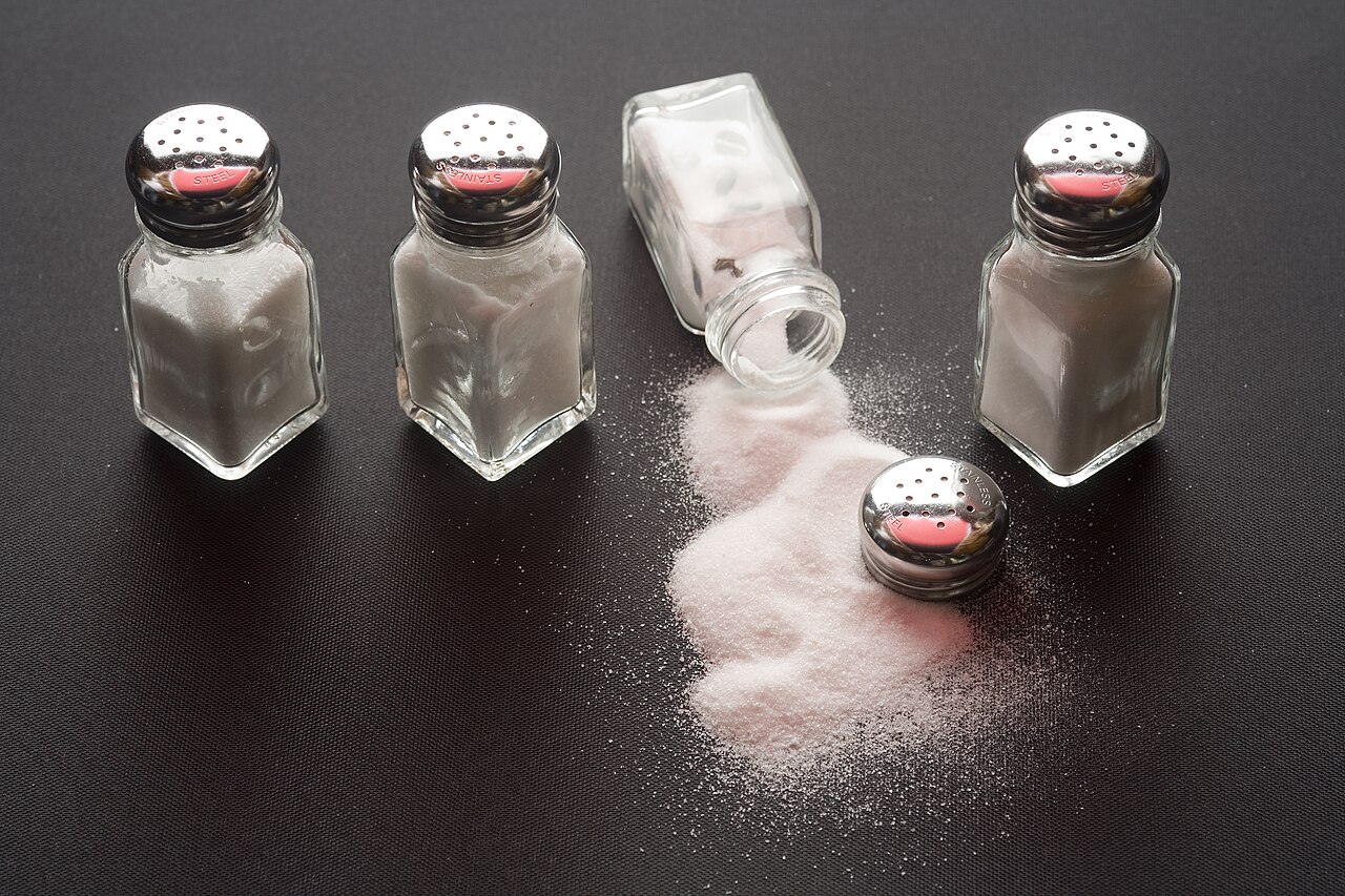 Four salt shakers on a table with salt spilled from one of them / Wikimedia Commons (File:Saleros - 5394.jpg)