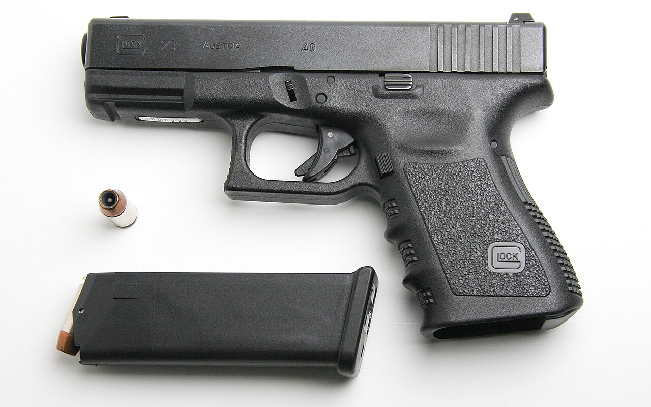 A Glock 23 Generation 3 handgun with a loaded magazine of .40 S&W hollow-point ammunition photographed against a white background / Public Domain