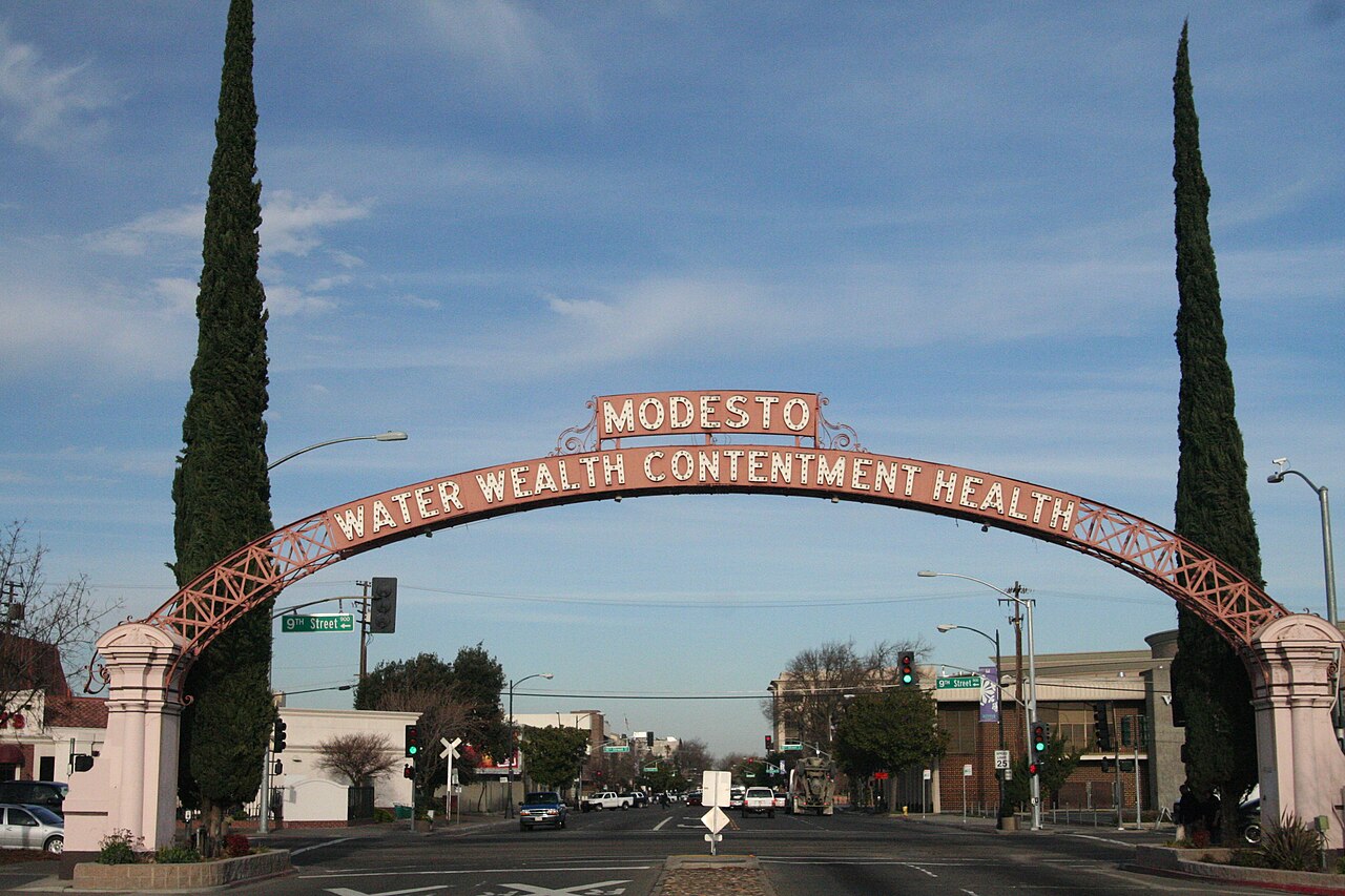 The Modesto Arch, a landmark monument in Modesto, California, with the city motto "Water, wealth, contentment, health" inscribed on it / By Level crossing, CC BY-SA 3.0, via Wikimedia Commons