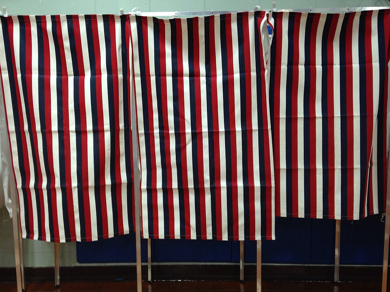 Voting stations inside a polling location in Ward 1 of Nashua, New Hampshire, showing the interior setup with voting booths and signage / Photo by an unknown photographer via Wikimedia Commons